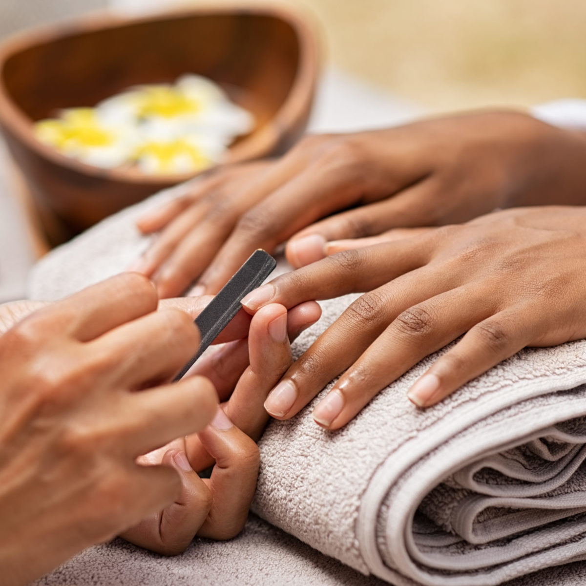 Close up of african woman hand getting manicure in spa salon. Detail of black hands getting manicure treatment at luxury spa. Girl in a nail salon receiving treatment by a beautician with nail-file.
