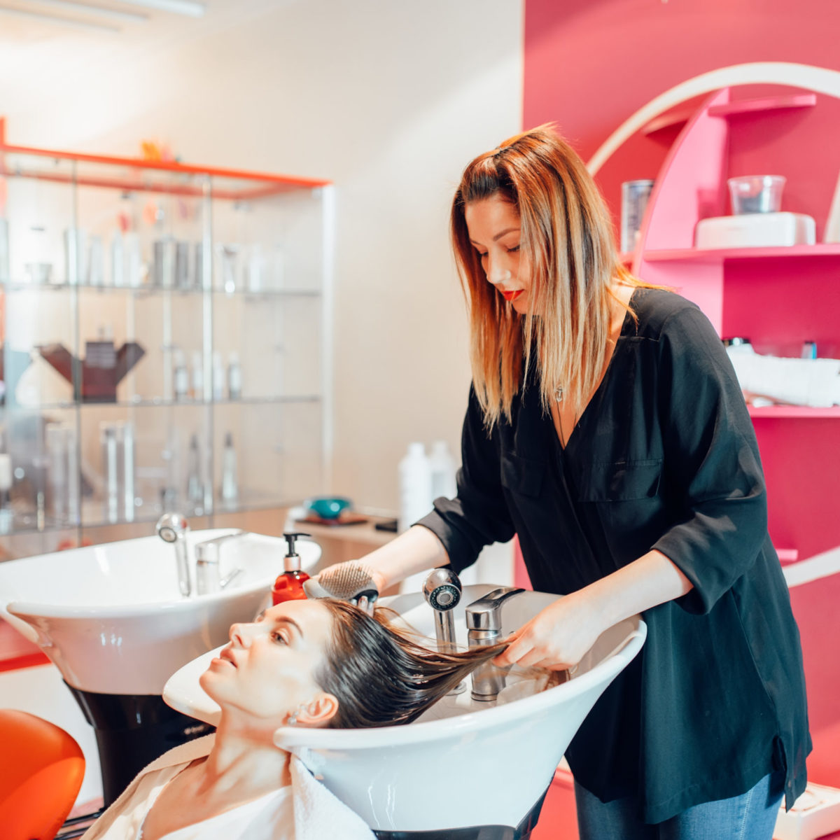 Hairdresser washes customer hair in hairdressing salon. Professional haircare in beauty studio, female client and beautician